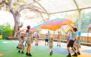 Primary school children gather around a parachute for play.